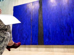 Big Blue painting by Clyfford Still as seen from behind woman with red shoes writing in a blank book